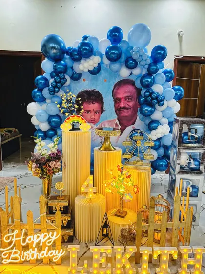 A personalized birthday setup featuring a custom backdrop with photos of the birthday boy and a loved one. The blue and white balloon arch and full prop display make it a heartfelt and memorable celebration.
