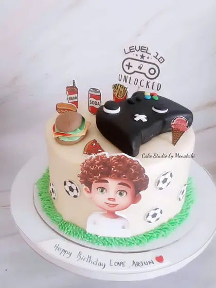 A gaming themed cake for a teenager. This design features a controller, junk food, and a caricature of the birthday boy.