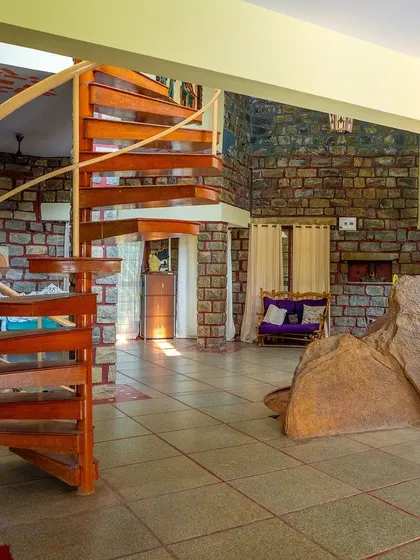 The main hall of the villa, showing the blend of natural rock, stone pillars, and the wooden spiral staircase.