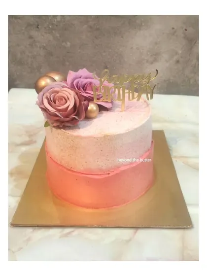 A simple and elegant birthday cake with a pink ombre design, topped with fresh roses and gold spheres.