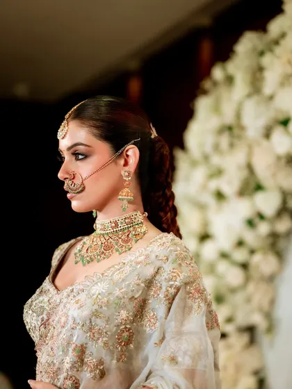A side profile that highlights the intricate hairstyle and the beautiful line of the jaw and neck. The makeup looks impeccable from this angle, showcasing a clean and polished finish.