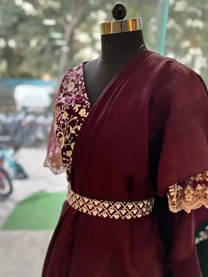 A closer look at the details of the wine-colored ruffle saree. The embroidered blouse features delicate floral work on one sleeve, and the embellished belt cinches the waist to create a flattering silhouette.