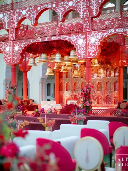 A closer view of the 'Kaanch Bagh' mandap, highlighting the contrast between the bold red structure and the elegant white and maroon seating. The design is deeply rooted in Indian culture and tradition.