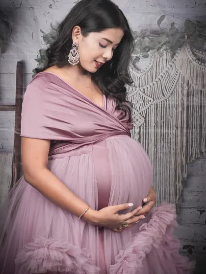A close-up portrait showcasing the details of a dusty pink ruffled gown. This studio shot against a boho backdrop highlights the soft fabric and flattering wrap-style top.