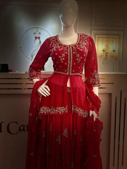 A mannequin displaying a beautiful red sharara set. The outfit features a peplum-style top with silver embroidery, paired with a layered sharara skirt.