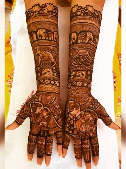 A classic bridal design featuring a couple's portrait on the palms. The forearms are decorated with auspicious symbols like elephants and kalash, bringing blessings and beauty to the bride.