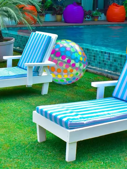 Classic poolside loungers with striped cushions, set up on the grass with colorful beach balls to complete the summer vacation vibe.
