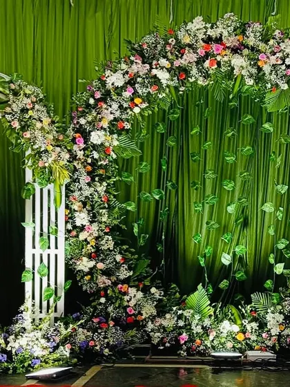 A lush and green engagement stage. The backdrop features a large floral arch with hanging leaves, flanked by smaller white arches, creating a beautiful garden-like setting.