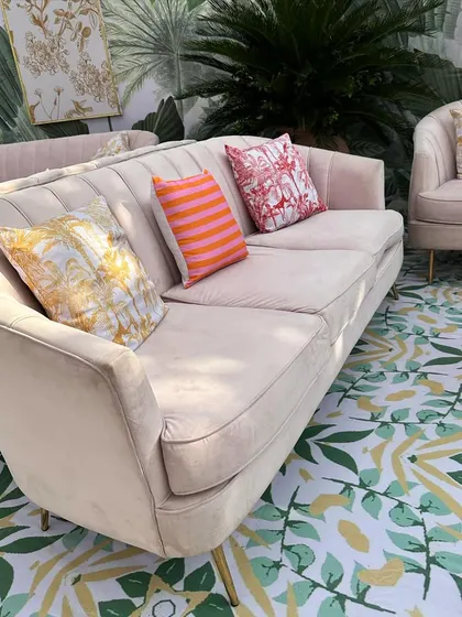 A plush, blush-pink sofa with colorful printed cushions sits on a custom floor with a green leaf pattern, creating a chic and comfortable lounge spot.