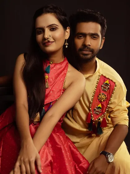 A close-up couple portrait against a simple black studio backdrop. This classic setup really makes their colorful, coordinated festive outfits stand out.