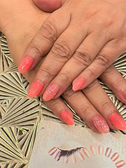 A lovely coral-colored set of almond nails. Two accent nails on each hand are covered in a fine, matching coral glitter for a cohesive and sparkly look.