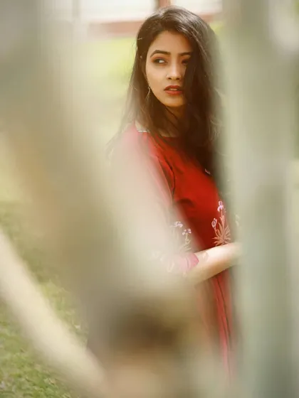 A vibrant color version of a shot framed by trees. The model's red dress stands out against the green foliage, and her thoughtful expression is captured in a way that feels candid and unposed, perfect for a lifestyle blog or personal branding.