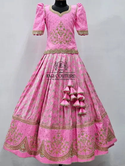 A grand, floor-length pink Banarasi lehenga. The entire outfit features heavy gold embroidery, a long side tassel, and a beautifully detailed blouse.