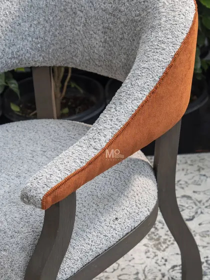 A close-up on the craftsmanship of the Versa Armchair. This detail shows the contrast between the soft bouclé, the corded orange accent, and the deep earthy brown finish of the solid ash wood frame.