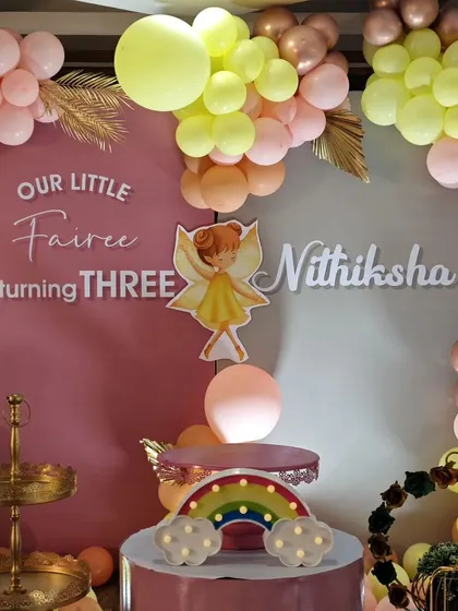 A detailed view of a 'Little Fairee' birthday setup, highlighting the custom name sign, cake stands, and a cute light-up rainbow prop.