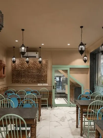 The dine-in space at Shiv Mishthan Bhandar features walls clad with lakhori bricks and traditional mouldings. Large glass panels create an interactive experience, connecting diners with the vibrant street life of Old Delhi.