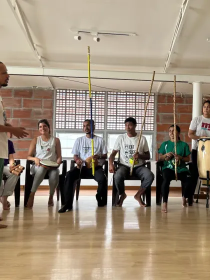 An instructor leads the 'bateria', the orchestra of the Capoeira roda. Students are learning to play the berimbau, atabaque (drum), and pandeiro.