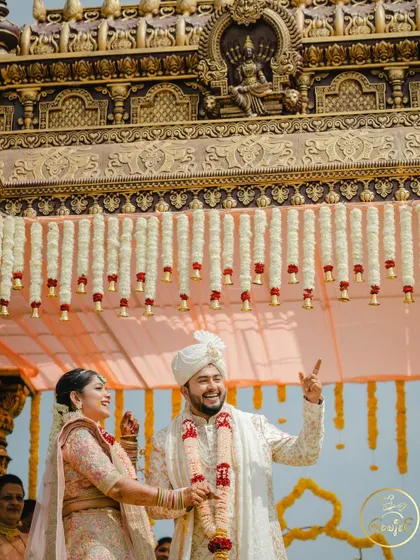 The couple looking joyful under their grand, temple-style wedding mandap.