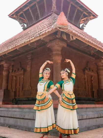 A wide shot of two dancers in front of a traditional temple structure. This image captures the grandeur of the dance form and its cultural context.