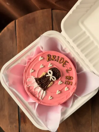 A perfect cake for a bridal shower or to celebrate a bride-to-be. This pretty pink bento cake is decorated with a drawing of a wedding dress and the words "Bride 2 Be," surrounded by tiny white hearts.