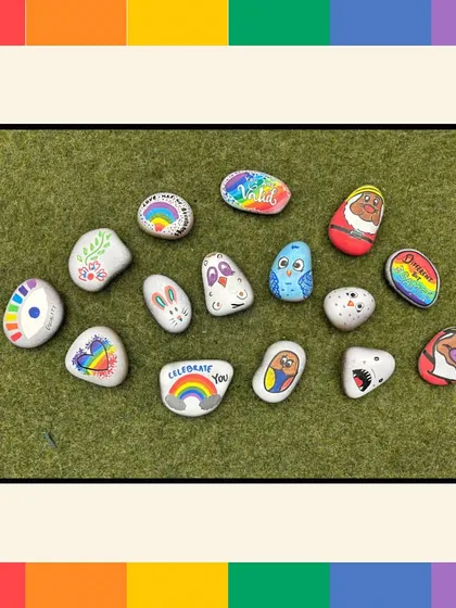 A collection of beautifully painted pebbles from our Pride workshop. Designs include rainbows, supportive messages like "Celebrate You," and other symbols of love and equality.