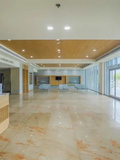 The main lobby of the Ranchi Cancer Hospital and Research Centre features high ceilings, marble floors, and large glass walls that connect the interior to the outdoors. This creates a bright, open, and welcoming atmosphere for arriving patients and visitors.