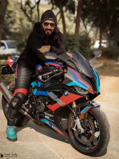 A rider posing with his stunning BMW M 1000 RR superbike. The colorful graphics of the bike are the star of the show, and the rider's pose exudes confidence and pride.