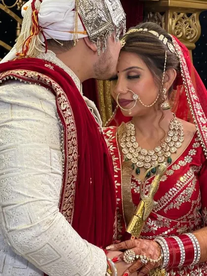 A perfect moment of love and blessings. The groom kisses his bride's forehead, and she looks serene and beautiful in her classic red bridal look.