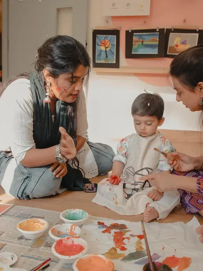 Two mothers guide a young child in a painting activity during our Holi event. This image showcases the collaborative and supportive environment we foster for both children and parents.