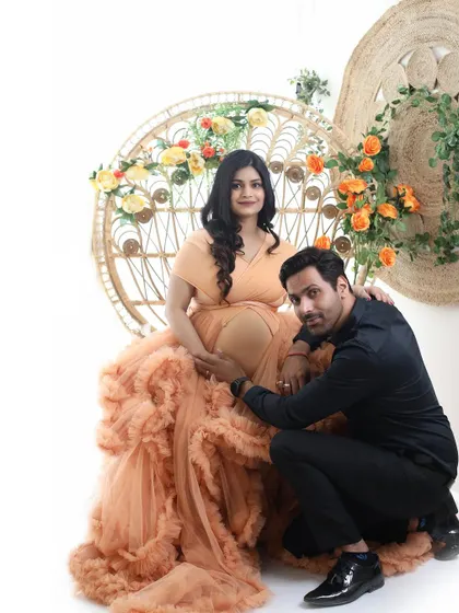 A classic pose where the dad-to-be kneels to connect with the baby bump. The mom-to-be is radiant in a peach ruffled gown, set against our bright and airy studio backdrop.