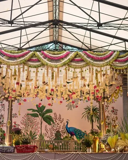 A full view of the traditional South Indian mandap, showcasing the intricate floral torans, classic temple pillars, and the beautiful hand-painted backdrop. We draped the ceiling in soft green fabric to complement the natural surroundings.