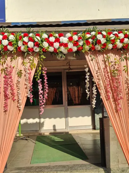 A simple and pretty entrance decoration with peach-colored drapes and a floral top piece. Perfect for house parties or small hall events.