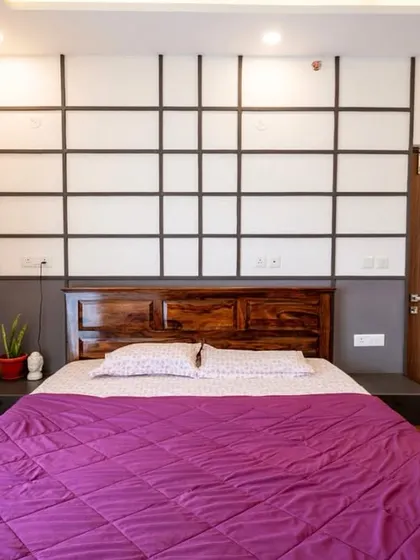 In this bedroom, a geometric accent wall with a grid pattern adds depth and character. The rich tones of the wooden headboard and flooring create a serene and inviting atmosphere.