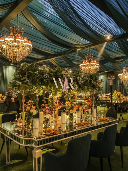 This long table was the centerpiece of the celebration, featuring a mirrored surface and an overhead floral installation. The design combines the glamour of chandeliers with the natural beauty of overflowing greenery and colorful blooms.