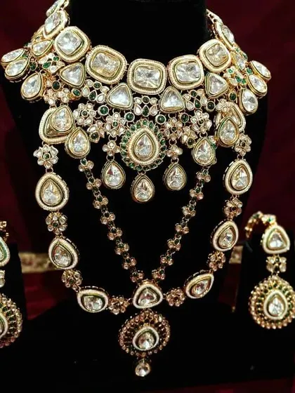 This is a grand, multi-layered Kundan necklace set with green stone accents. It includes a choker and a longer necklace for a complete, royal look.