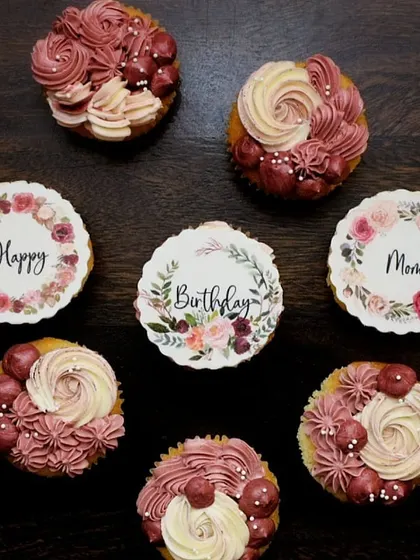A beautiful floral-themed set to wish a happy birthday to a client's mom. The box mixes cupcakes with delicate pink and white buttercream piping and others with elegant, printed floral wreath toppers.