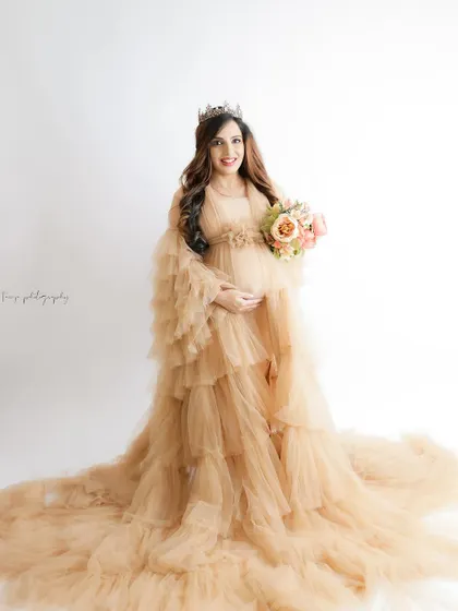 A fairytale portrait in a flowing nude-colored gown. The mom-to-be wears a tiara and holds a bouquet, looking like a princess.