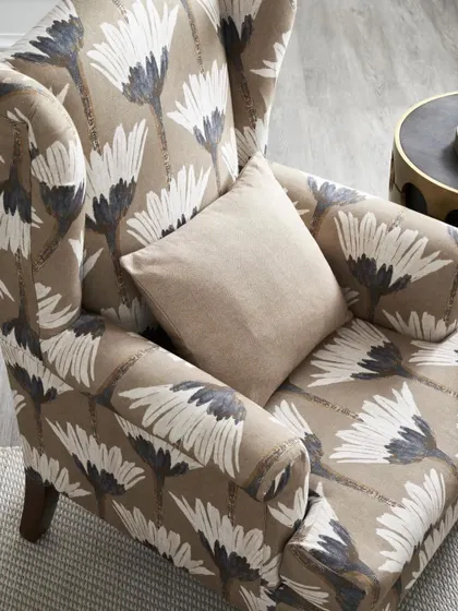 A detail shot of a wingback chair upholstered in a bold floral print. The focus is entirely on the fabric's pattern and how it wraps around the chair's classic form.
