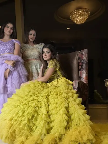 A group of models showcasing my collection of multi-layered ruffle and frill gowns. The yellow gown with its long, textured trail is a standout piece for a mehendi or pre-wedding shoot.