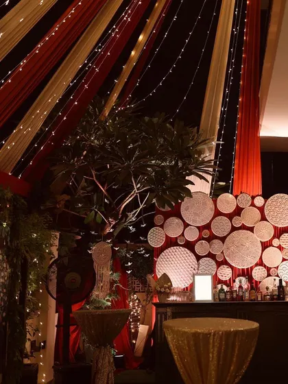 The bar area for our autumn-themed party. A custom backdrop of white woven discs contrasts beautifully with the red and gold draped ceiling, which is strung with fairy lights.