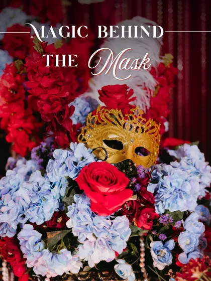 The magic behind the mask. This centerpiece, featuring a golden mask nestled in red and blue florals with pearl and feather accents, perfectly captured our luxurious Masquerade theme.