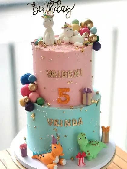 The full view of the two-tiered cake for twins, combining a unicorn theme on top and a dinosaur theme on the bottom.