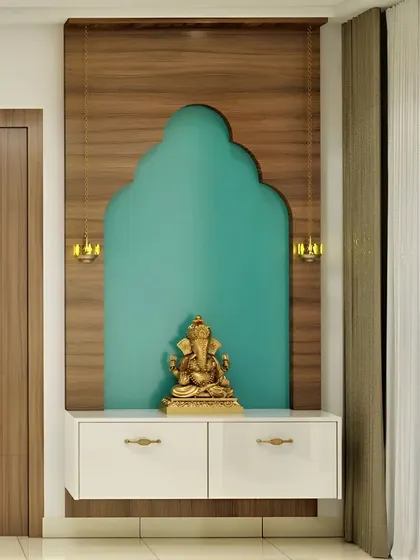 This minimalist pooja corner uses a bold teal accent wall shaped like a traditional arch to create a striking focal point. A simple white floating cabinet and two hanging lamps provide a clean, uncluttered space for a Ganesha idol.