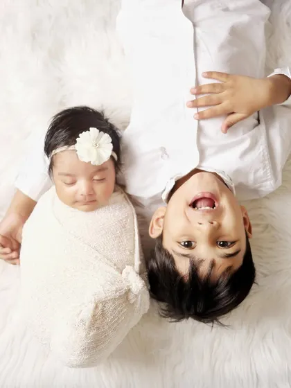 A fun, creative angle for a sibling photoshoot. This top-down shot captures the playful and loving connection between a big brother and his newborn sister.