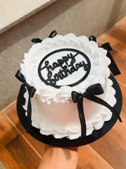 A chic black and white birthday cake. The design features piped ruffles and delicate black satin bows.
