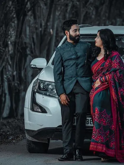 A modern pre-wedding portrait featuring the couple with their car. The selective color effect highlights the bride's saree against the monochrome background, adding an artistic touch to the shot.