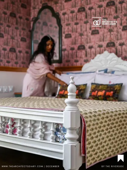 A guest bedroom featuring a bold Sabyasachi wallpaper, a refinished white heirloom bed, and the designer adding the final touches.