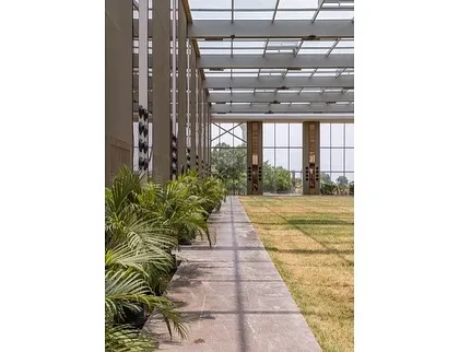 The design ensures a seamless transition between the built structure and the natural earth. A row of indoor plants lines the edge, further softening the boundary between the interior lawn and the glass enclosure.