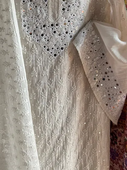 A close-up composition showing the texture of the Chikankari embroidery alongside the sleeve's mirrorwork and the edge of the vibrant Kashmiri Kalamkari fabric.