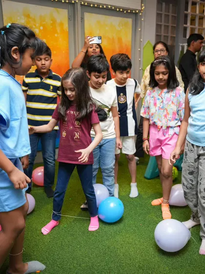 A fun balloon-popping game in progress. The kids are focused and ready to stomp on the balloons tied to their friends' ankles.